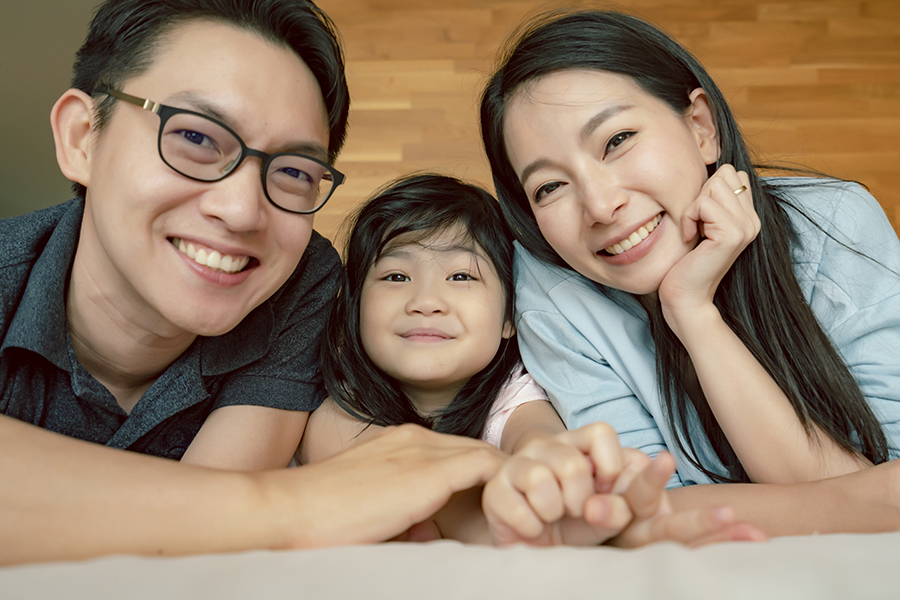 Insurance Quote - Joyful Family Portrait of Mom, Dad, and Daughter Laying Down in Bed of Their Family Home